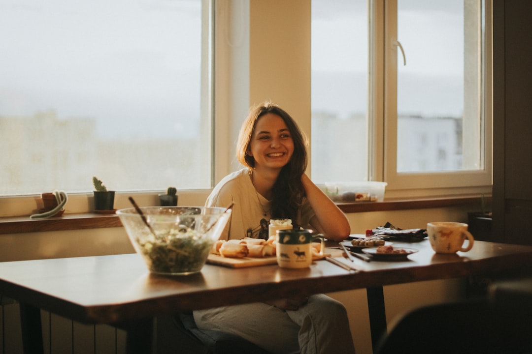A person sits at a kitchen table with a laptop, a phone, and stacks of insurance documents, looking focused on navigating a home insurance claim.
