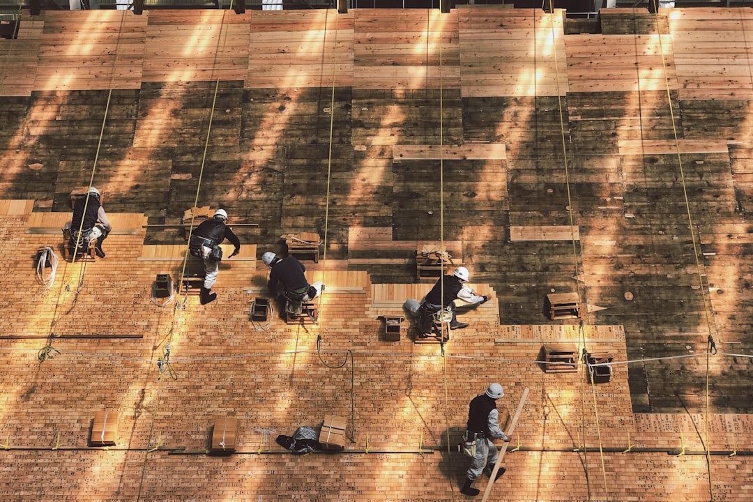 A professional roofer carefully installs new shingles on a residential roof against a clear blue sky, symbolizing the final step of a successful repair.