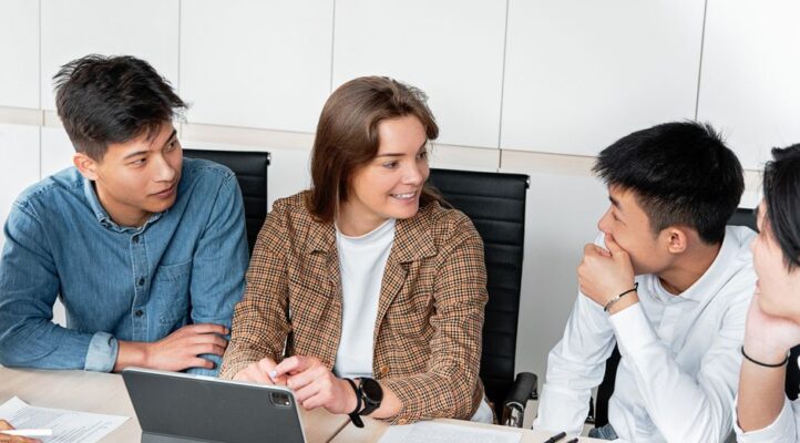 Diverse team of professionals in a bright, modern office collaborates around a table, reviewing documents and a tablet for...