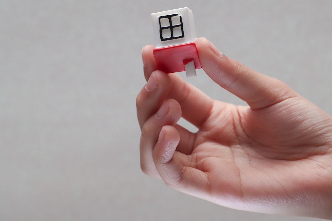 A pair of hands gently holding a small, simple wooden model of a house against a clean, bright background, representing care and expertise in achieving homeownership.
